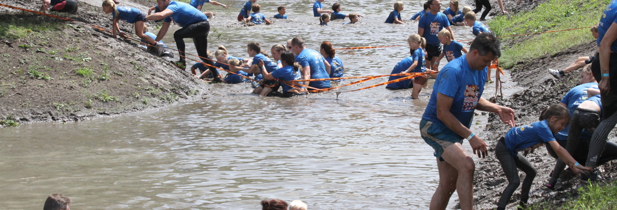 Deelnemers aan de Obstacle Run vervolgen hun parcours door de sloot. 