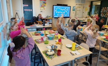 Kleine kinderen dansen in de klas dichtbij een mooi gedekte tafel voor het ontbijt.