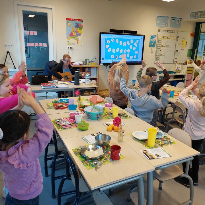 Kleine kinderen dansen in de klas dichtbij een mooi gedekte tafel voor het ontbijt.
