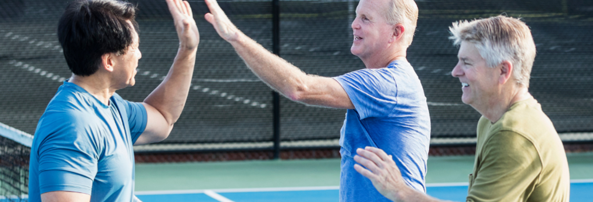 Volwassen mannen geven elkaar een high-five boven een tennisnet