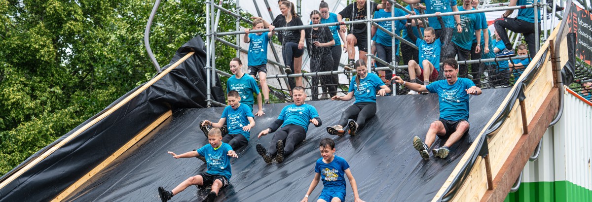 Deelnemers glijden van een grote glijbaan tijdens de Obstacle Run (fotocredit  Rosoriginal)