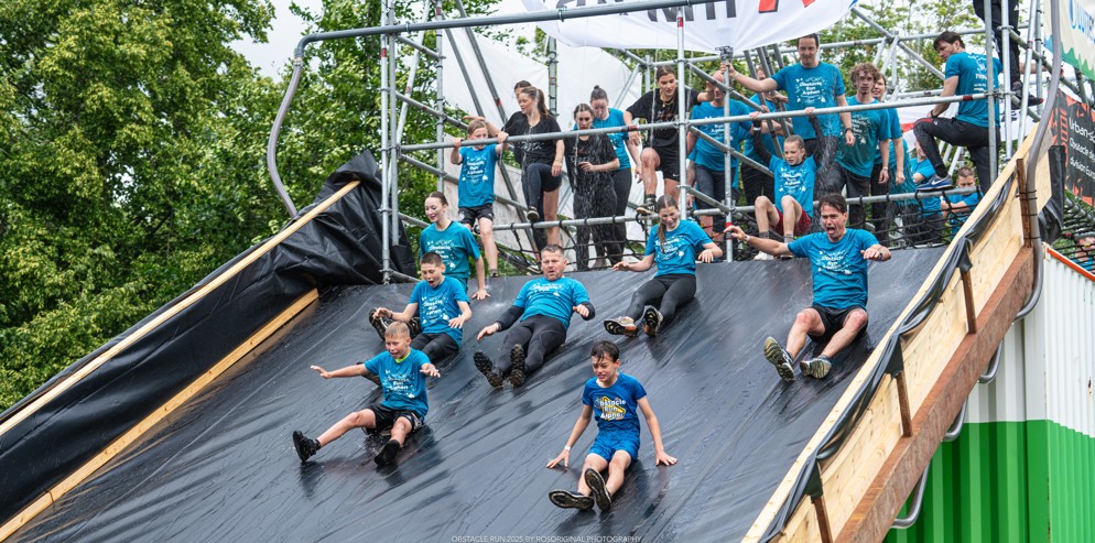 Deelnemers glijden van een grote glijbaan tijdens de Obstacle Run (fotocredit  Rosoriginal)