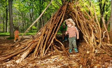 Een klein kind speelt in een zelfgemaakte hut in het bos.