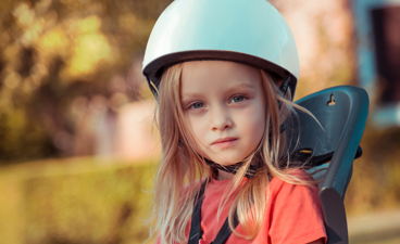 Een klein meisje zit achterop de fiets in een kinderzitje. 