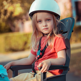 Een klein meisje zit achterop de fiets in een kinderzitje. 
