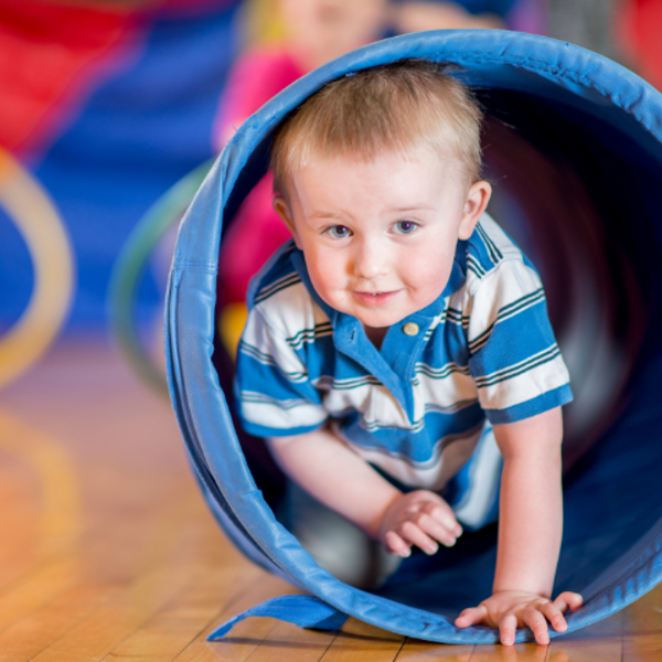 klein kindje kruipt door een speeltunnel tijdens de gymles.